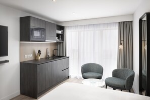 A modern kitchen with dark cabinetry, a microwave, and a small dining area with two chairs and a table. - Residence Inn by Marriott Manchester Piccadilly (Manchester)