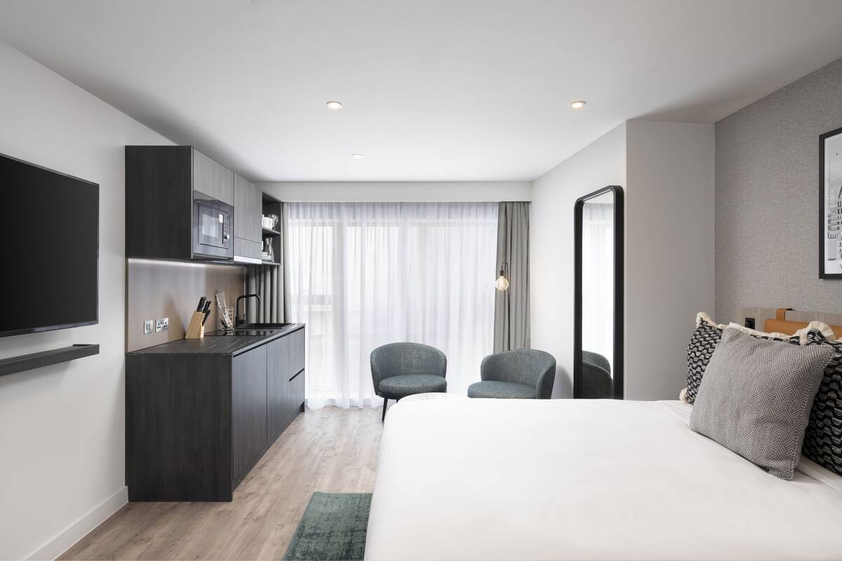 A modern hotel room with a bed, a desk with a flat-screen TV, a chair, and a large mirror.