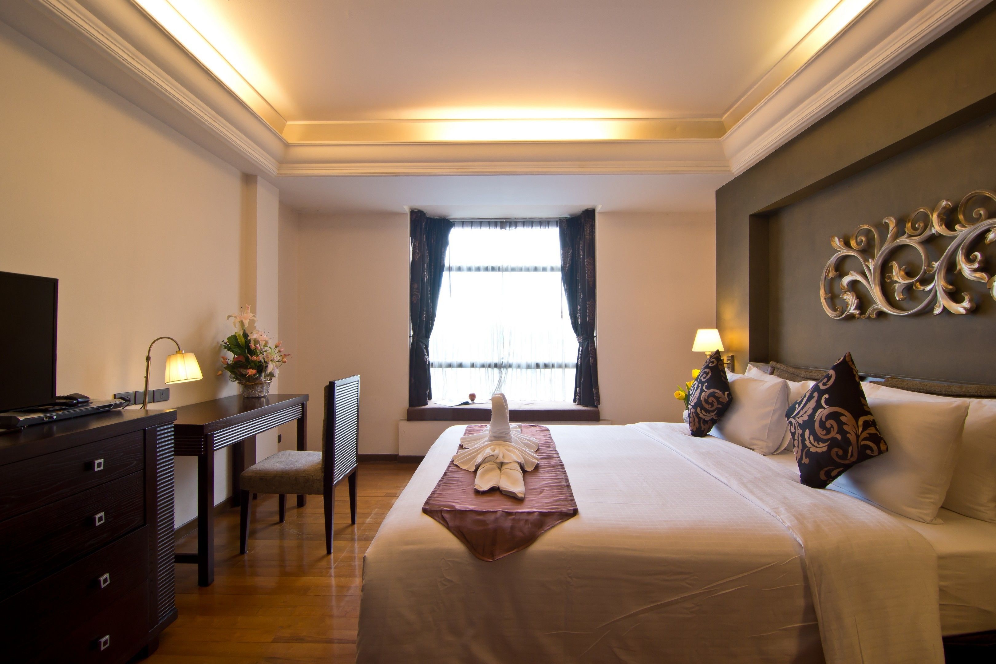 A hotel room with a bed, a desk, a chair, a TV, and a window with curtains.