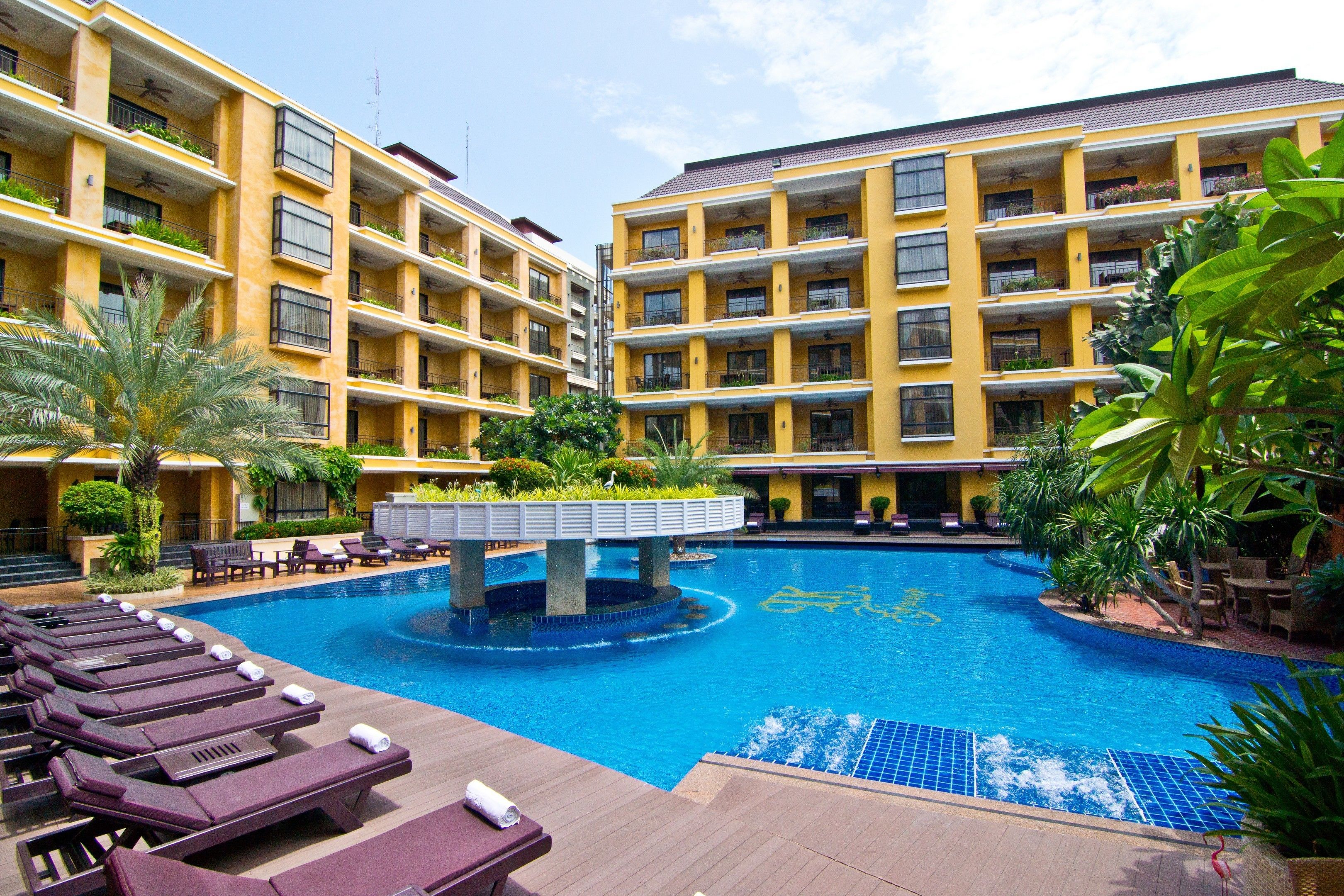 A hotel with a central swimming pool surrounded by lounge chairs and a bridge.