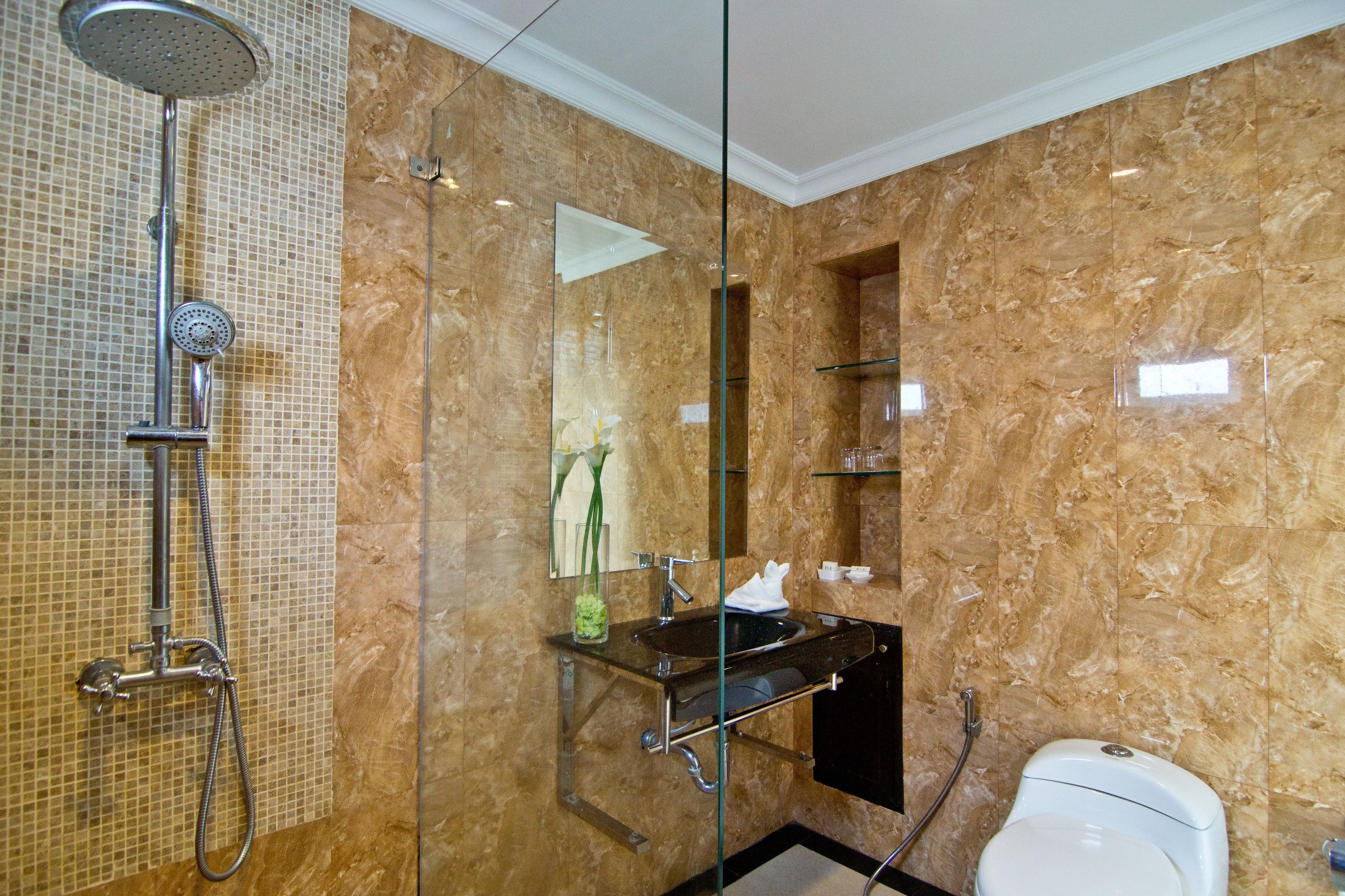 Ein modernes Badezimmer mit einer gläsernen Duschkabine, einer marmorierten Wand, einem schwarzen Waschbecken und einer Toilette.