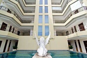 A multi-level hotel interior with a central atrium, a statue, and a pool. - LK Residence (Pattaya)