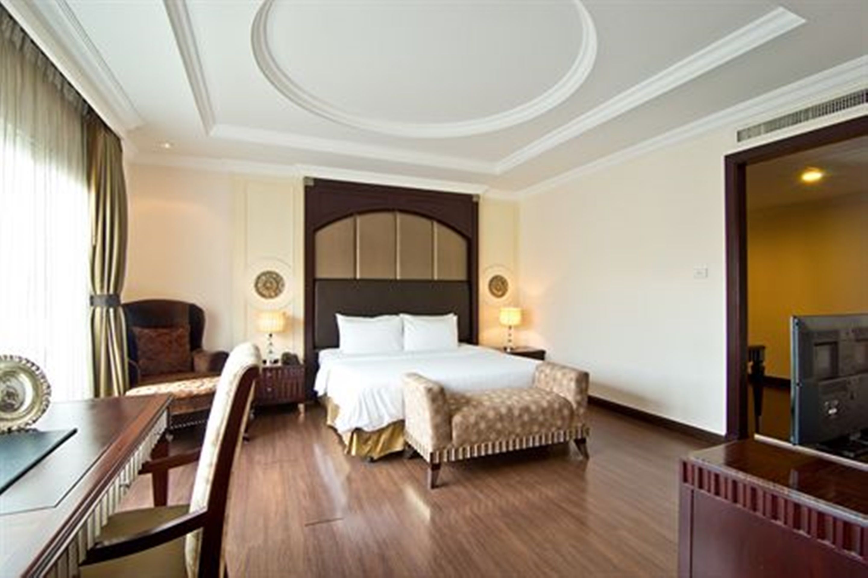 A hotel room with a large bed, a desk, a chair, a television, and a wardrobe.