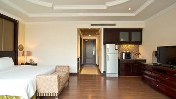 A hotel room with a bed, a sofa, a TV, a kitchen area with a microwave, and a refrigerator.