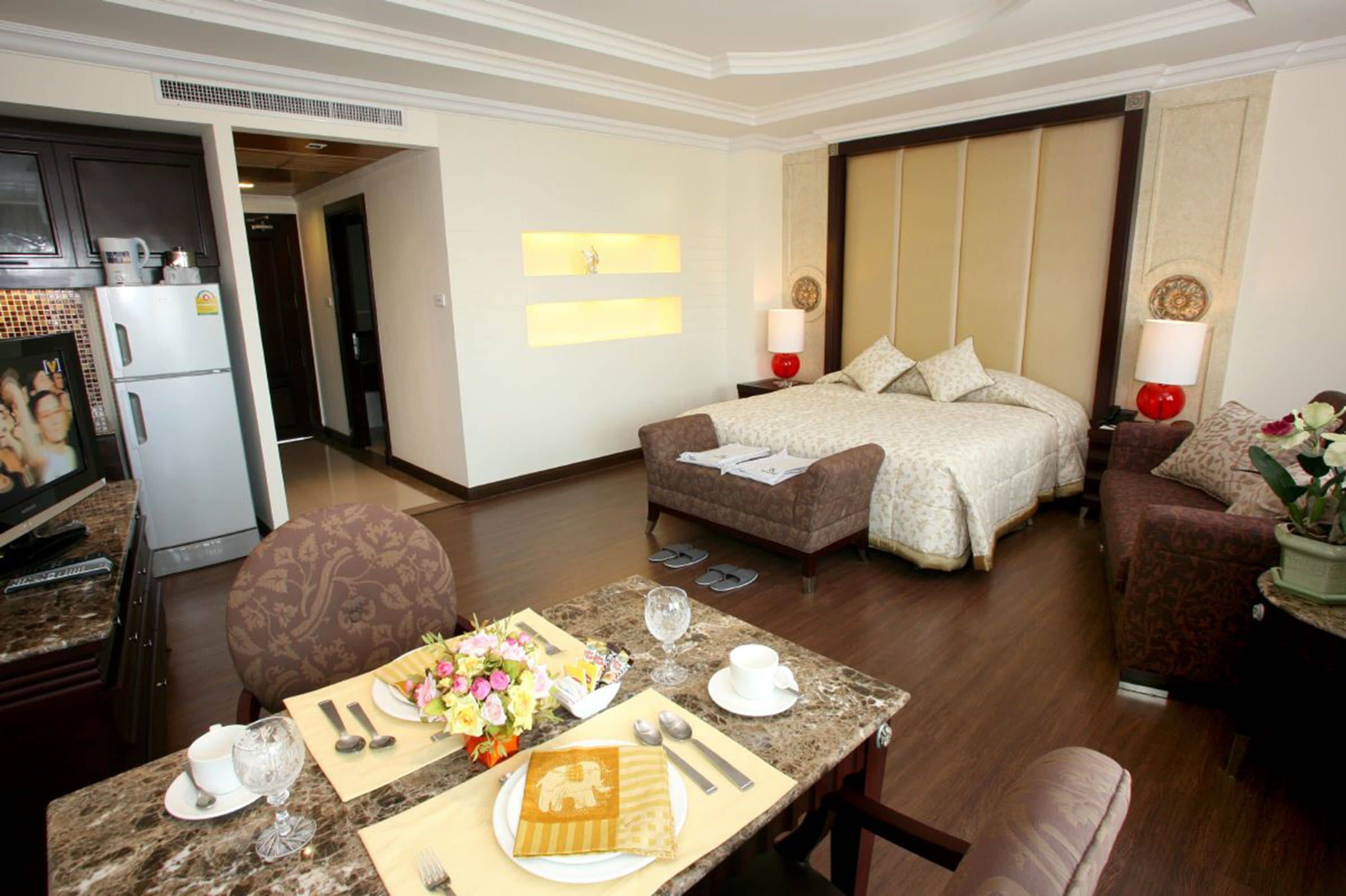 A hotel room with a bed, a sofa, a dining table set with a meal, and a kitchen area with a refrigerator and microwave.
