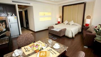 A hotel room with a bed, a sofa, a dining table set with a meal, and a kitchen area with a refrigerator and microwave.