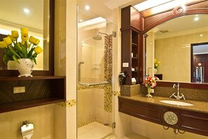 A bathroom with a glass-enclosed shower, a sink with a mirror, and a vase of yellow flowers on the counter. - LK Residence (Pattaya)