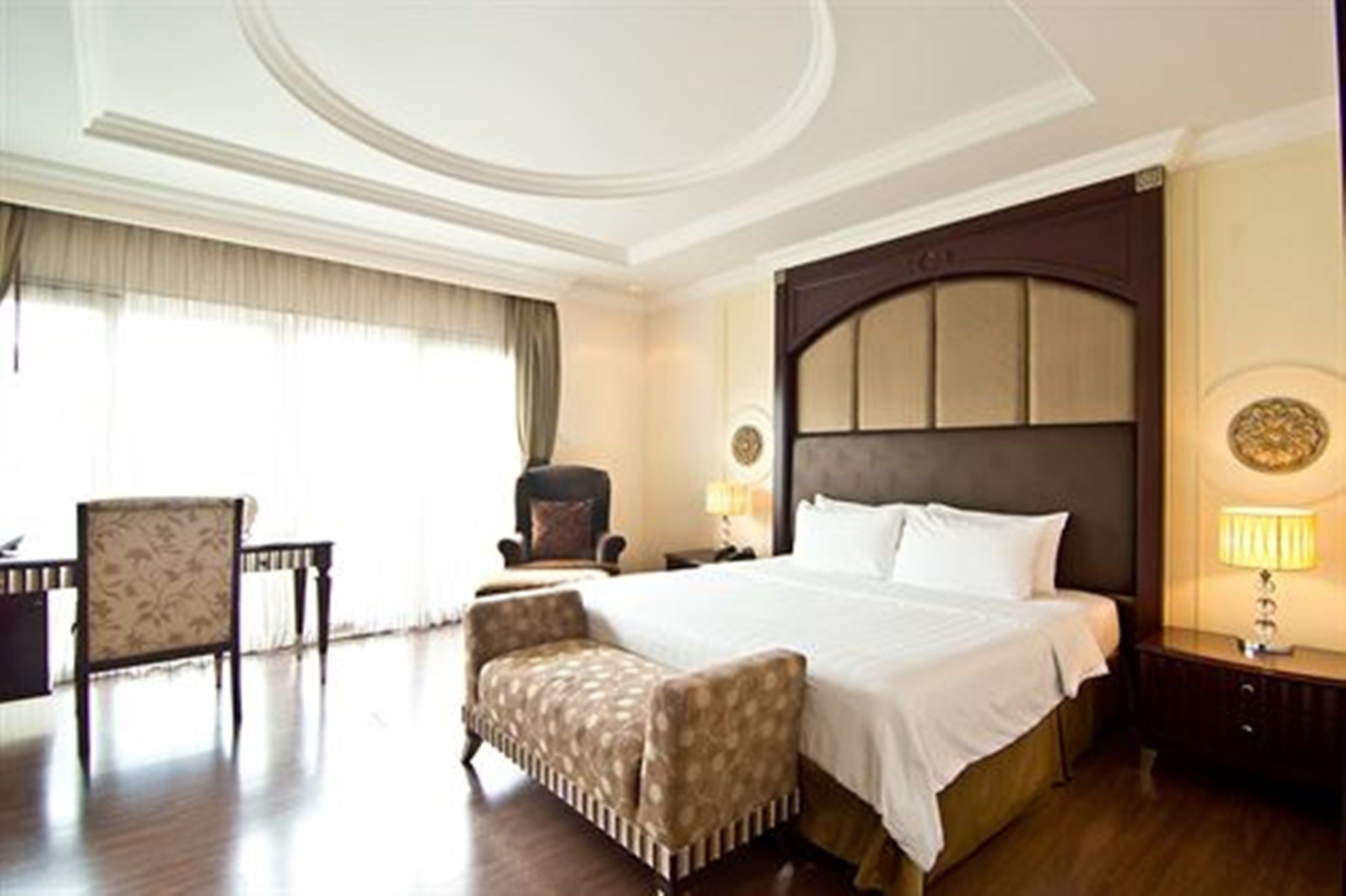 A hotel room with a large bed, a chair, a desk, and a lamp.