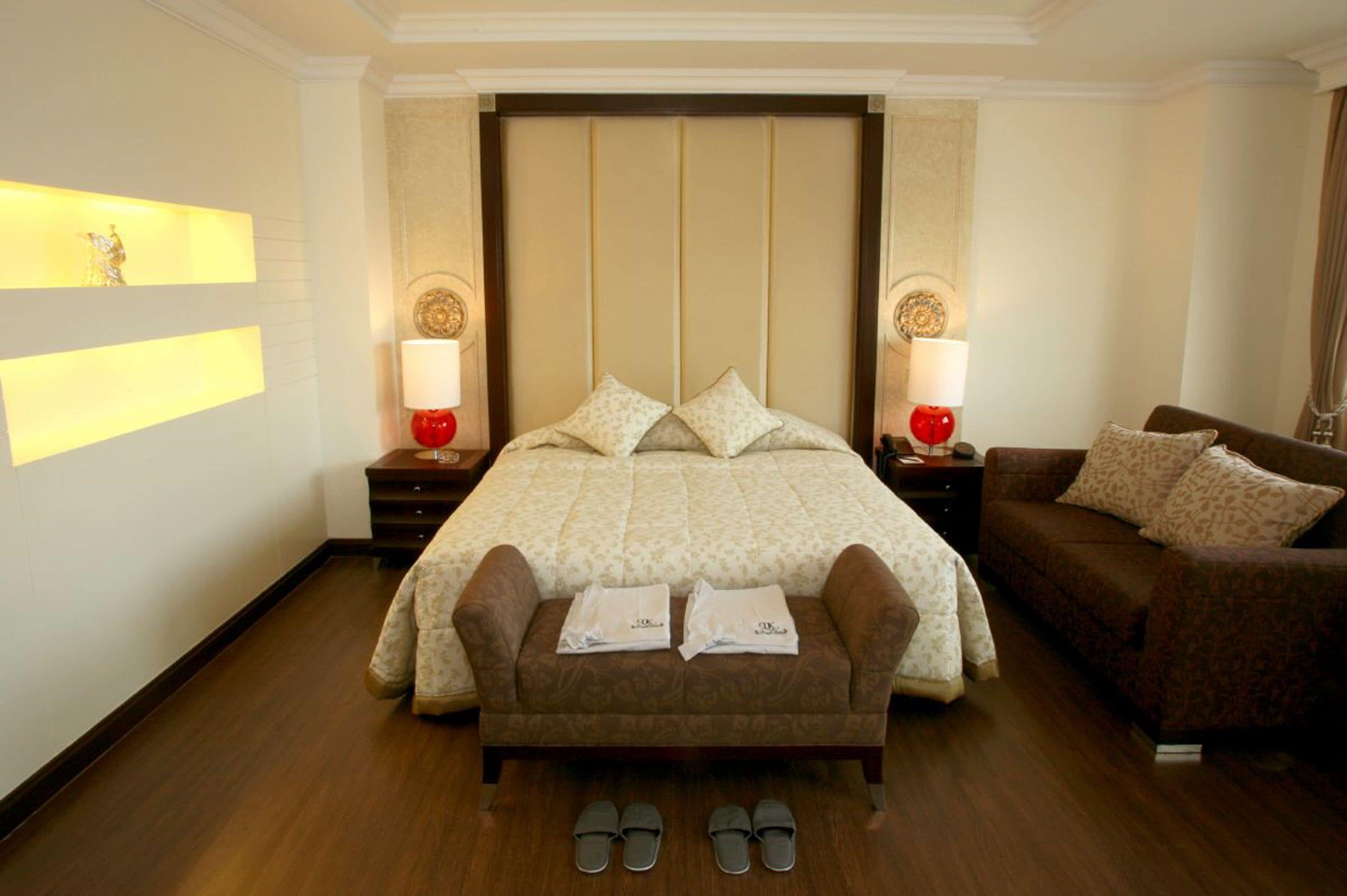 A hotel room with a large bed, two bedside tables with lamps, a brown sofa, and a small table with two towels.