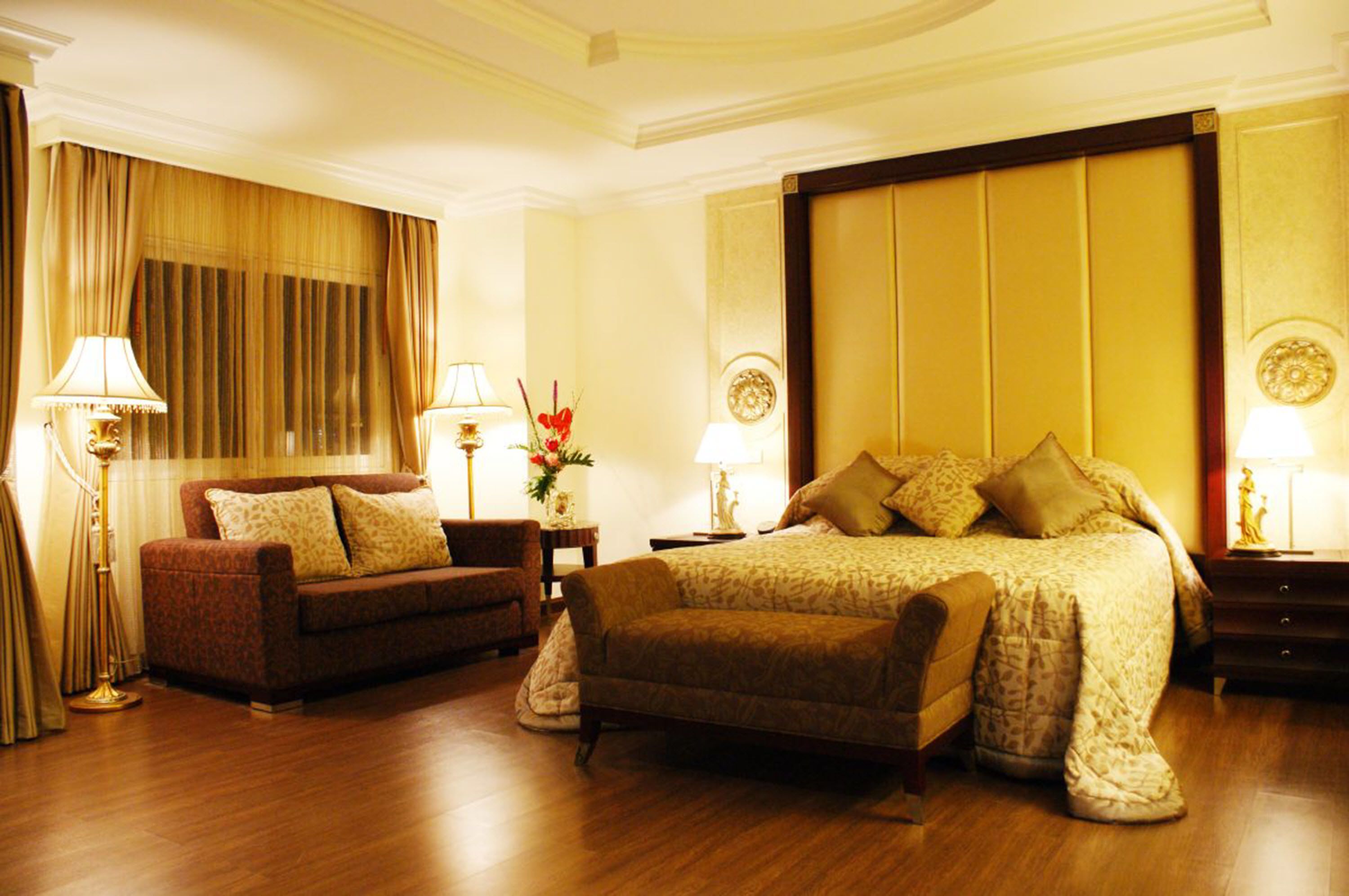 A hotel room with a large bed, two armchairs, a nightstand, a lamp, and a window with curtains.