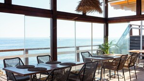 Comedor con vista al océano, con sillas de mimbre, una mesa de madera y una planta en maceta.