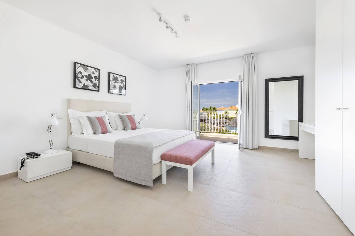A modern bedroom with a large bed, bedside table, and a view of the outdoors through a sliding glass door.