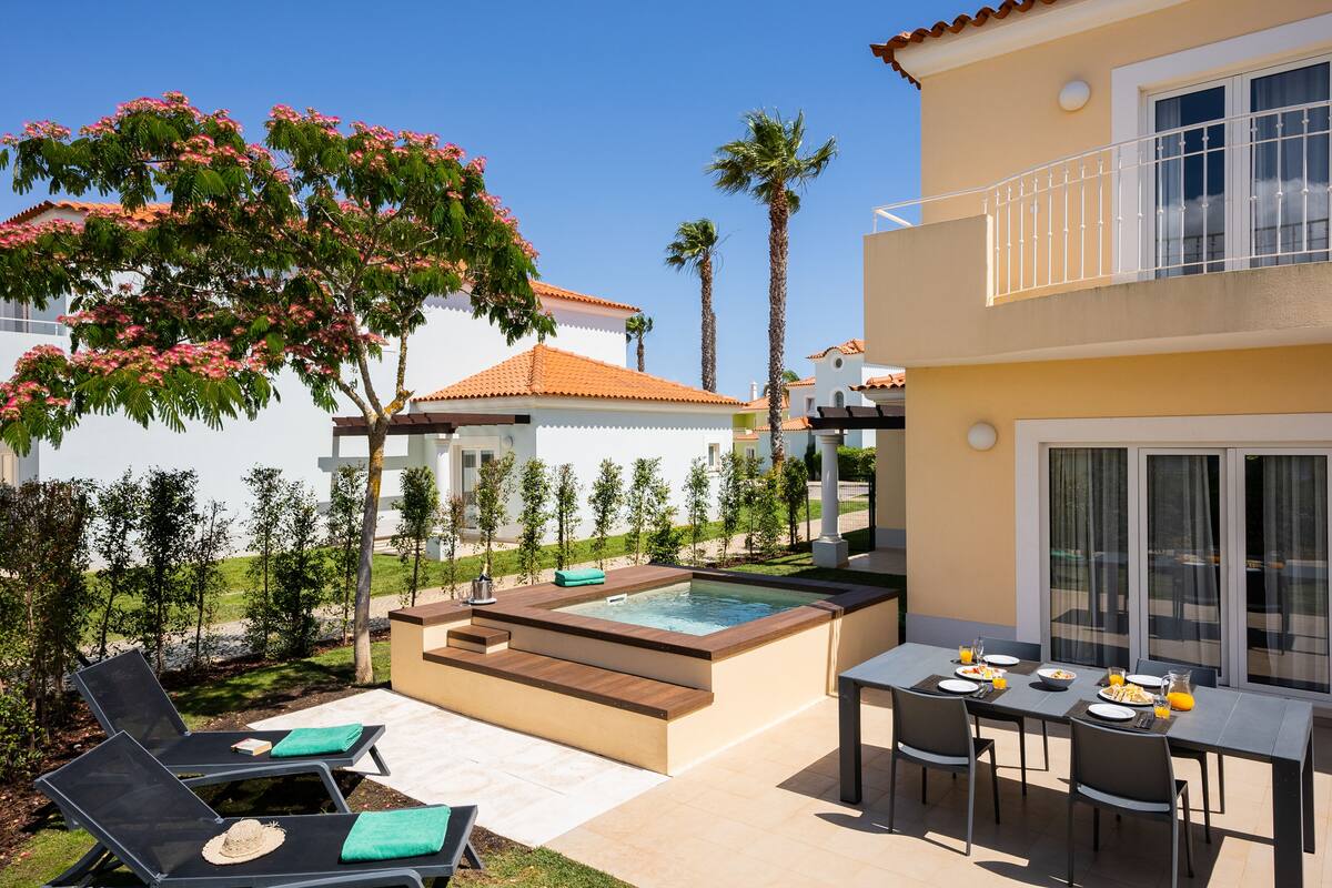 A poolside area with a hot tub, lounge chairs, and a dining table with chairs.