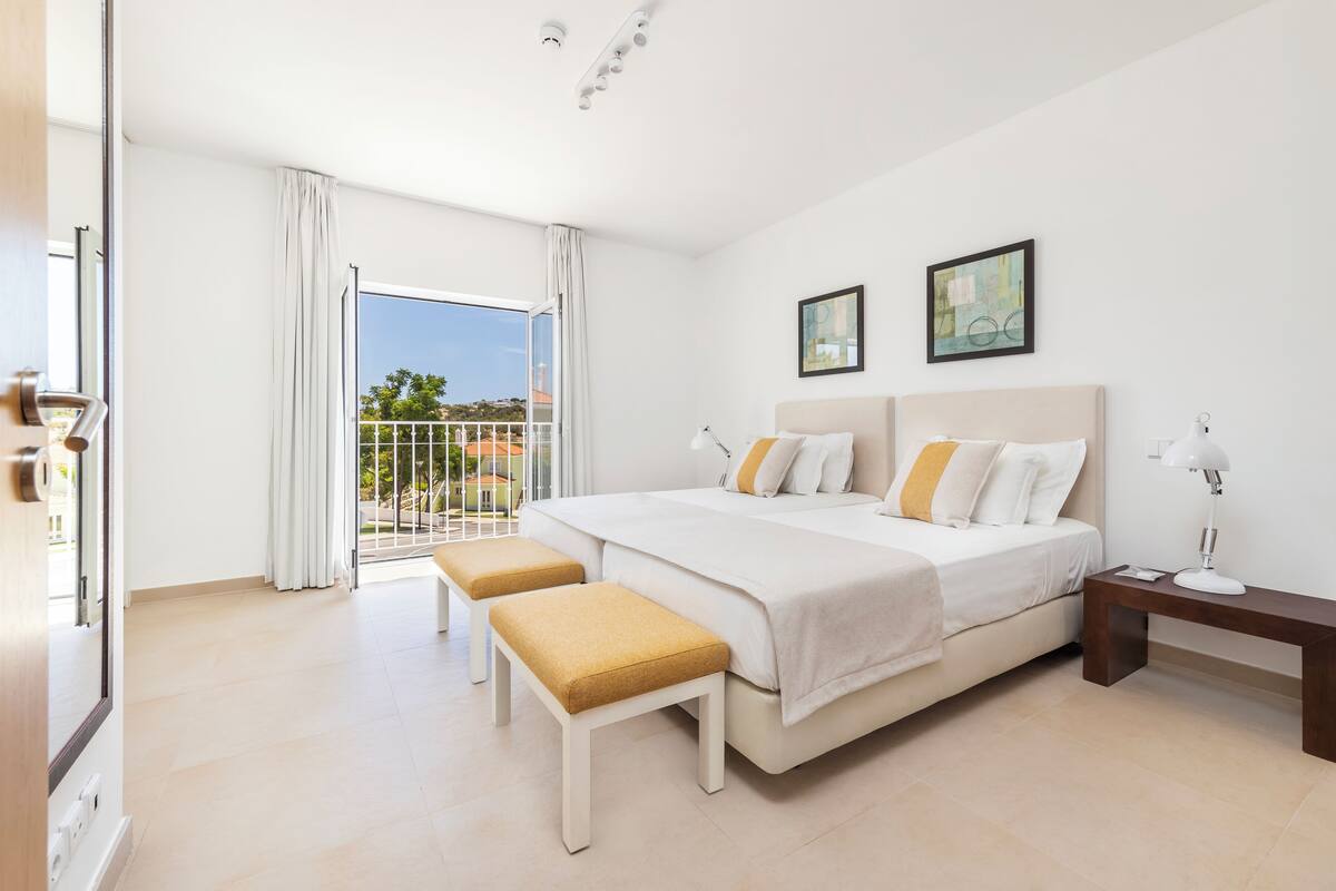 A modern hotel room with a large bed, two bedside tables, a bench, and a balcony with a view.