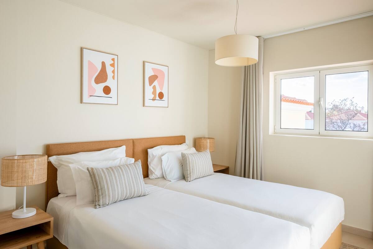A hotel room with a large bed, two bedside tables, a lamp, and two framed abstract paintings on the wall.
