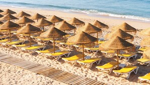 Una playa con filas de tumbonas y sombrillas de paja.