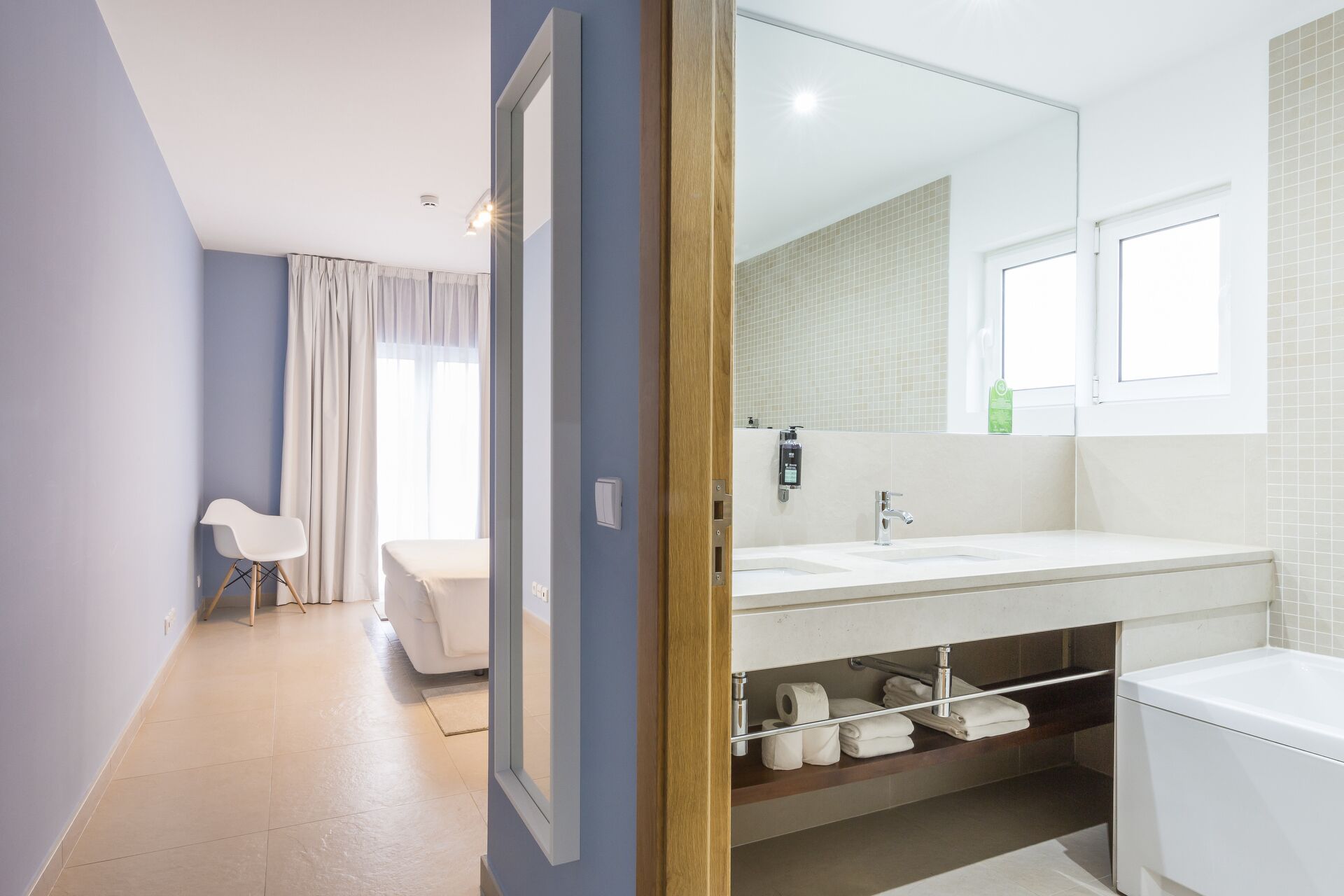 Un baño moderno con un espejo grande, lavamanos blanco y estantes empotrados.
