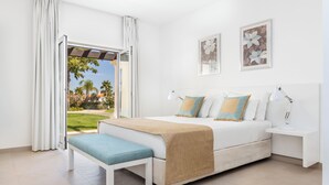 Un dormitorio con una cama grande, un banco, una mesita de noche y vistas a un jardín.