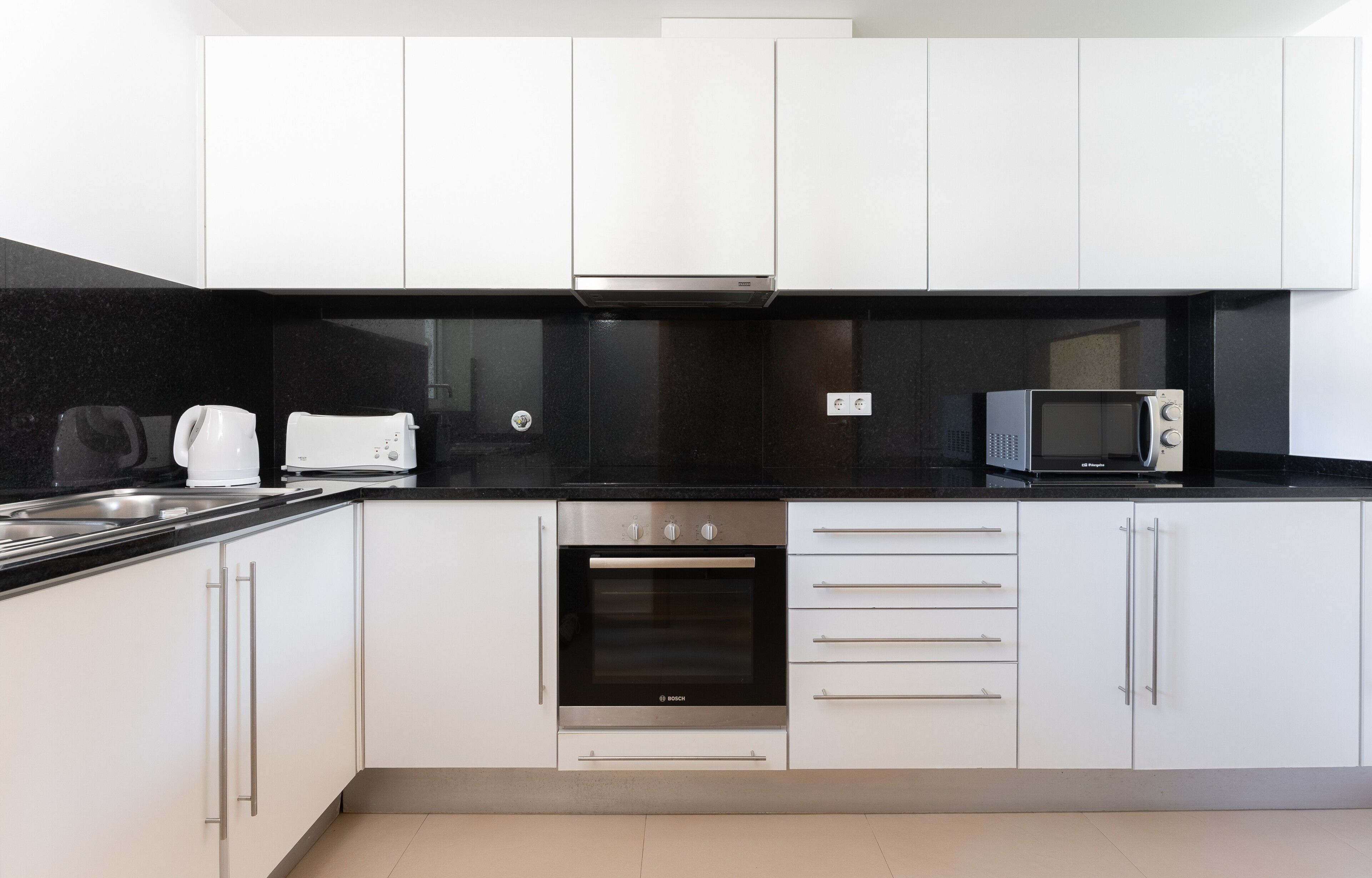 A modern kitchen with white cabinets, a black countertop, a Bosch oven, a microwave, and a coffee maker.