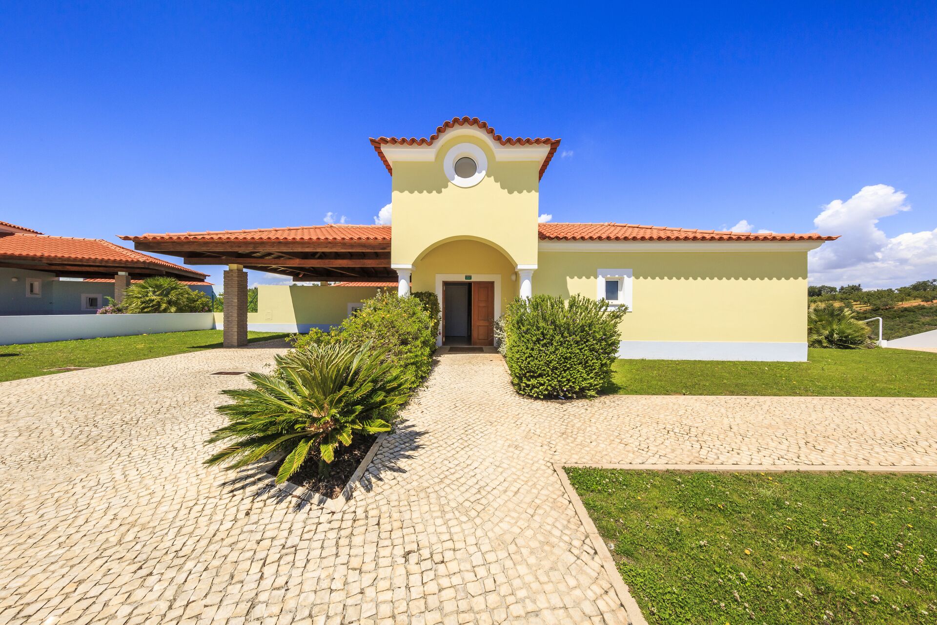 A two-story building with a red-tiled roof, a central archway entrance, and a paved driveway leading to the entrance.