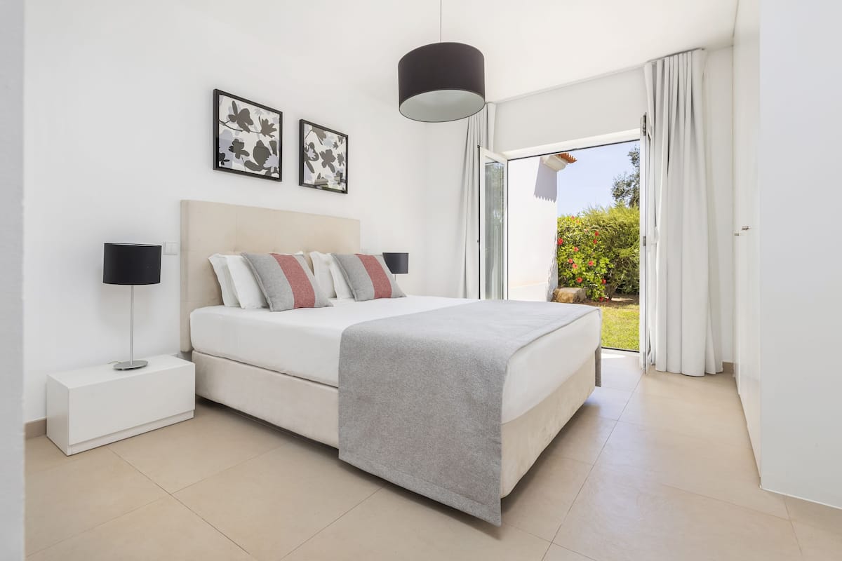 A modern bedroom with a bed, bedside tables, and a view of the outdoors.