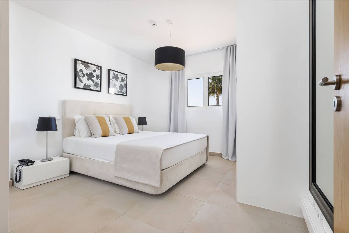 A modern bedroom with a bed, bedside tables, a lamp, and artwork on the wall.