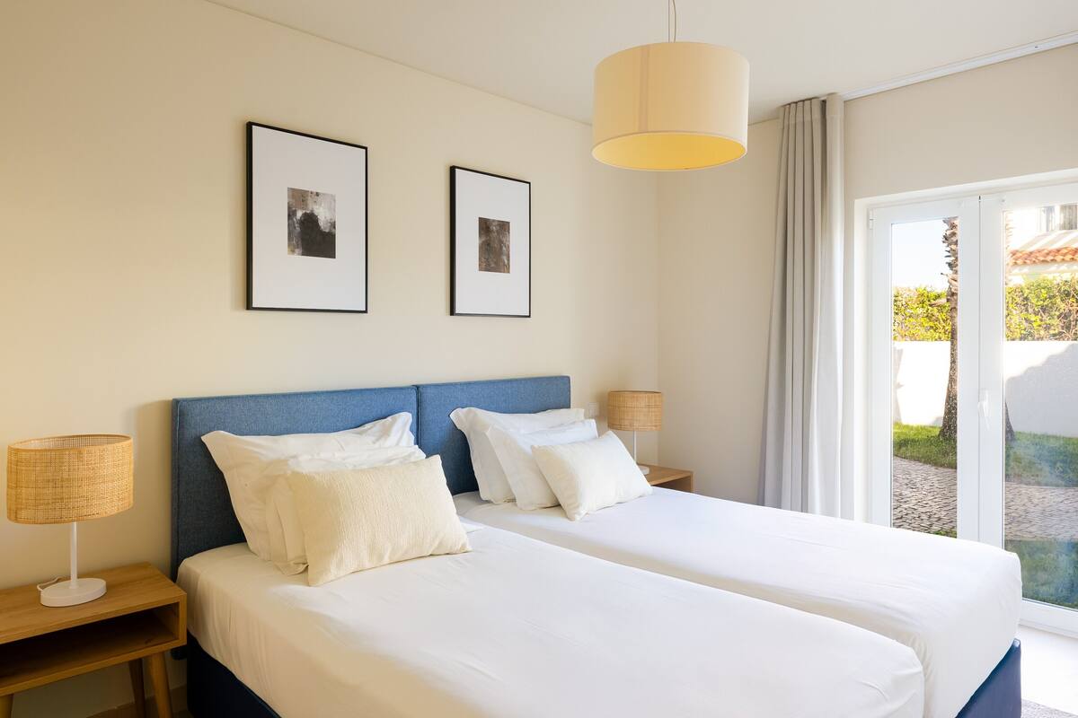A hotel room with two beds, a large window with a view, and two framed pictures on the wall.