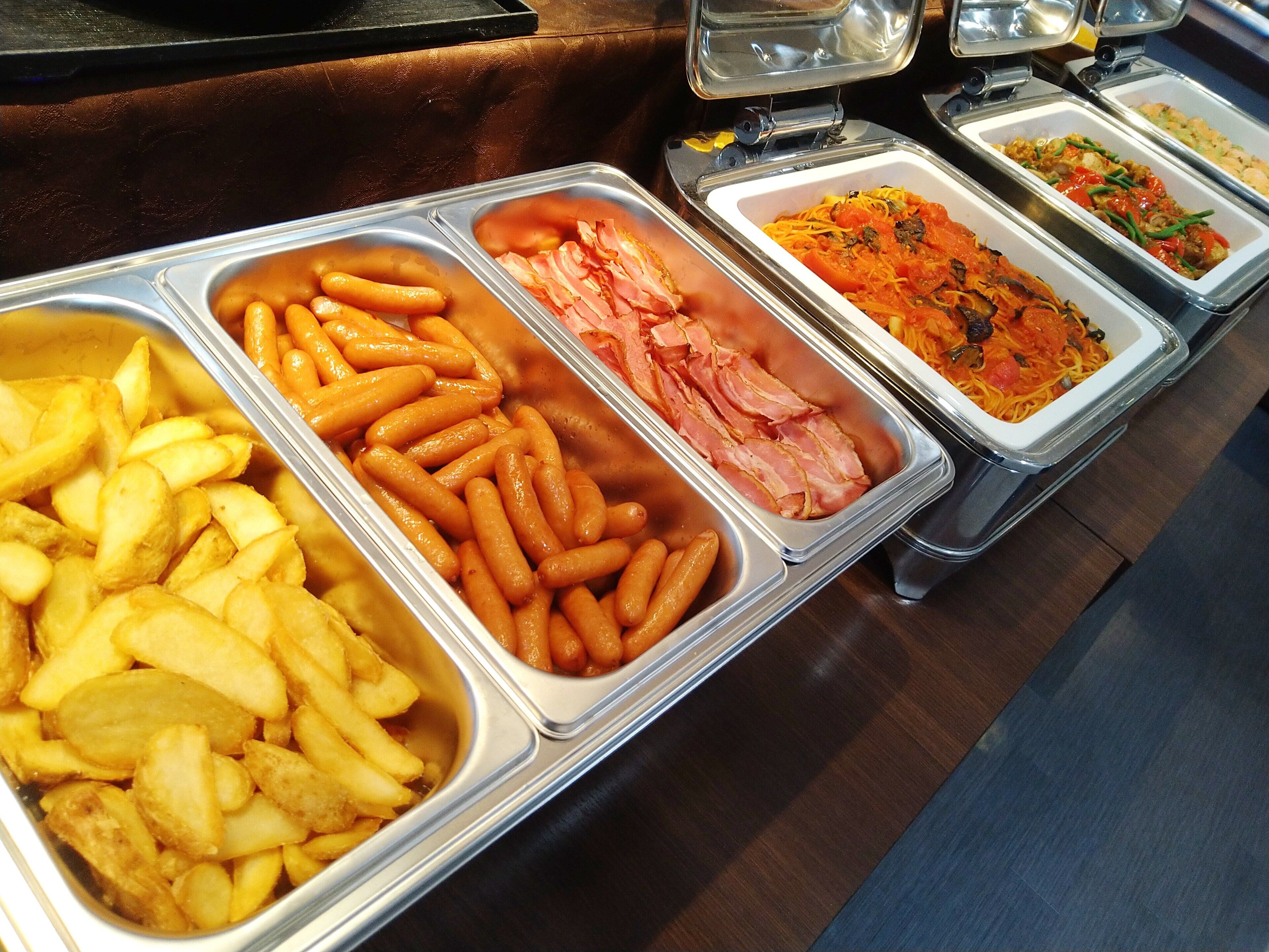 A buffet with various food items including French fries, sausages, and pasta.