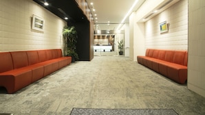 A modern lobby with two rows of orange seating, a reception desk in the background, and a patterned carpet. - Hotel Grand City (Tokyo)