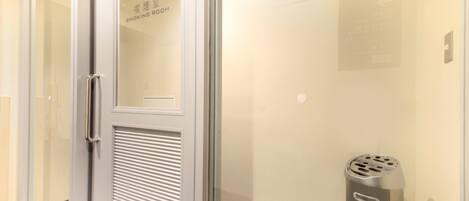 A hotel room with a sliding door leading to a smoking room, a trash bin, and a wall-mounted sign.