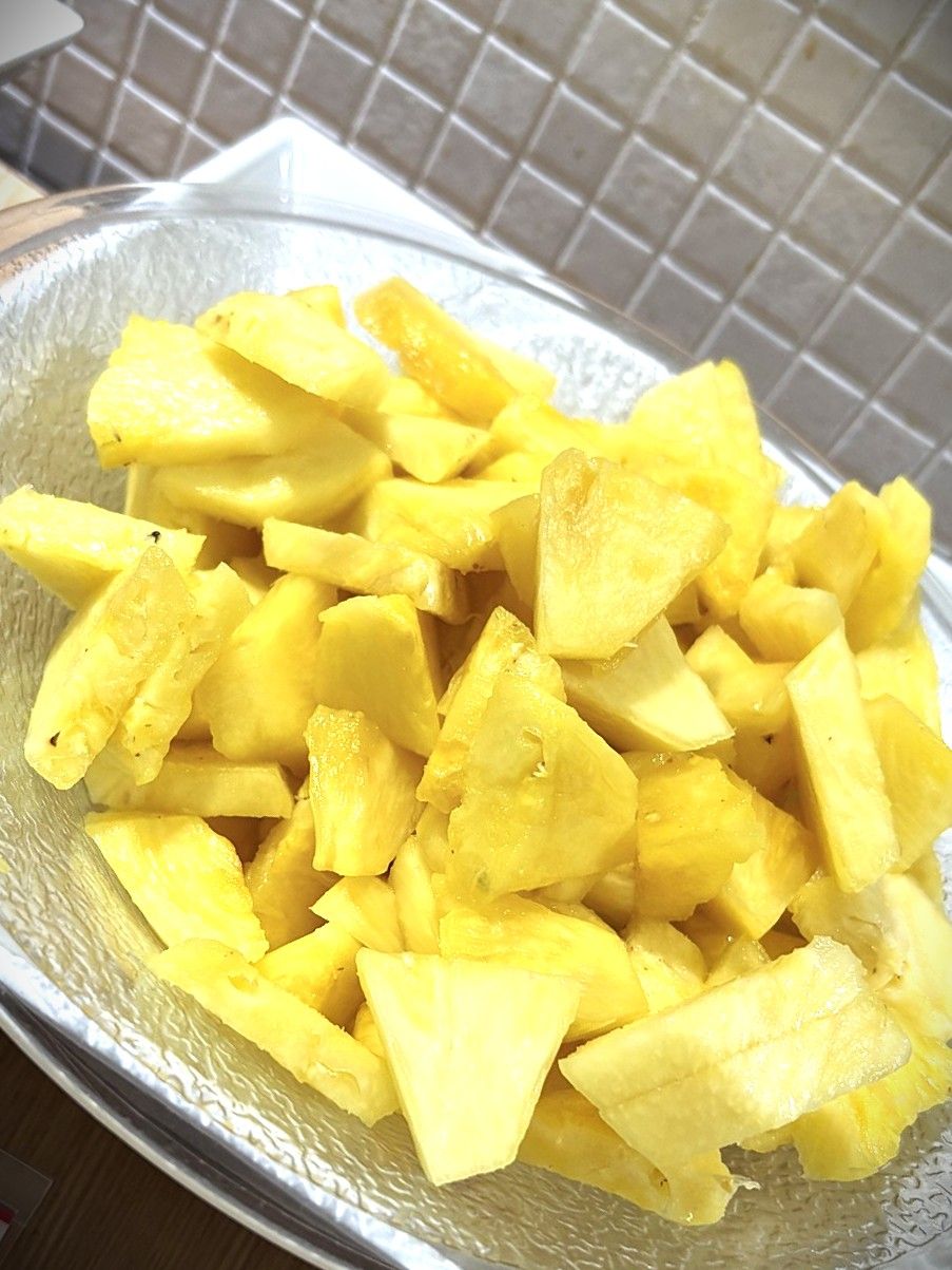 A bowl of diced yellow fruit, likely pineapple, on a textured surface.