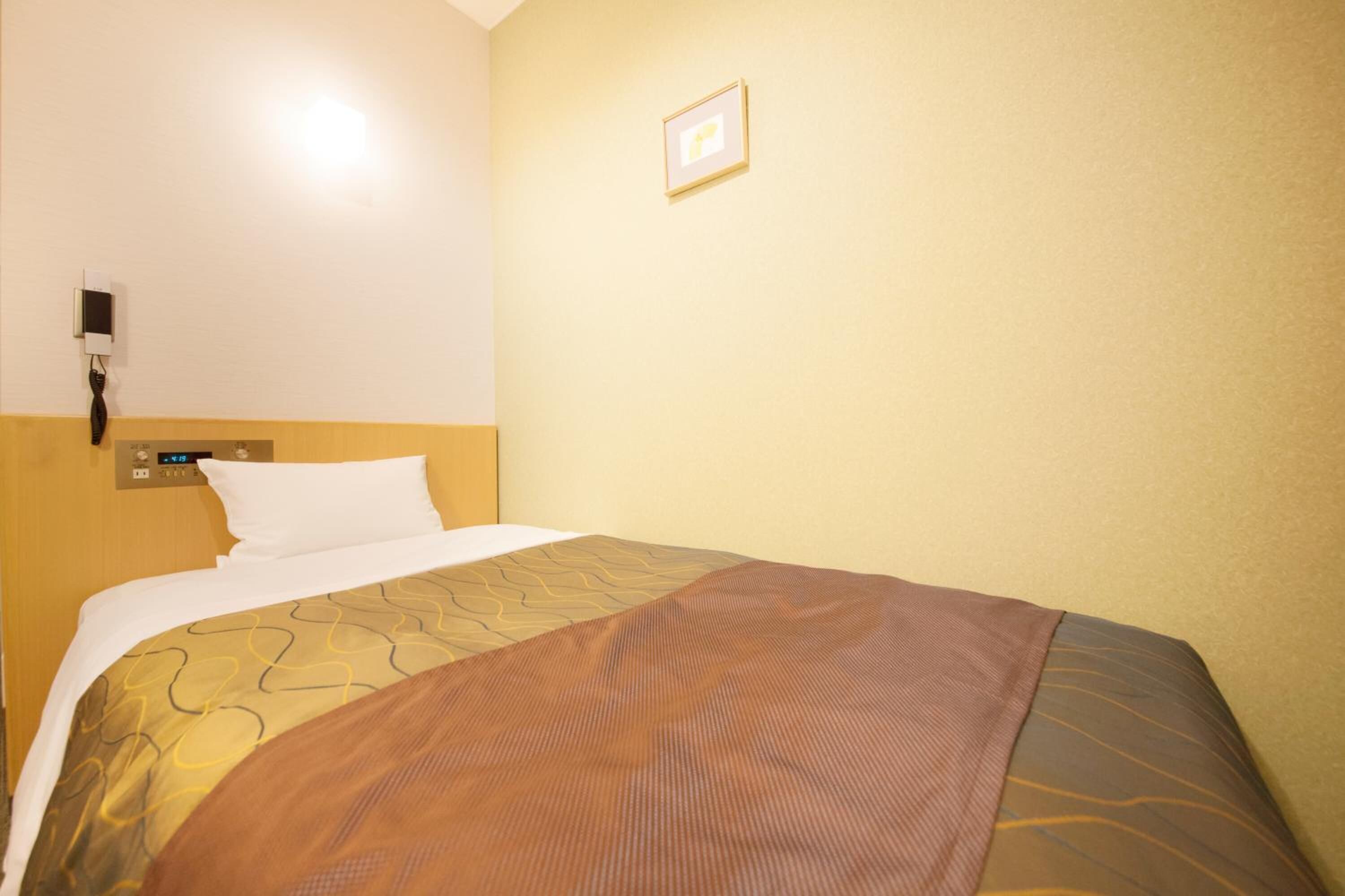 A hotel room with a bed, a wall-mounted phone, and a small framed picture.