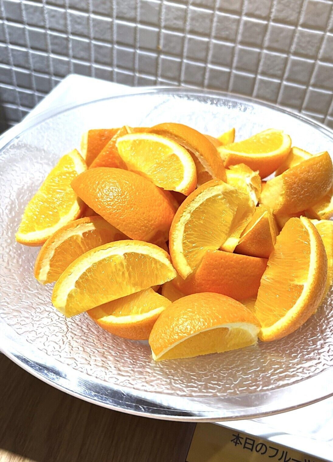 A bowl of orange slices on a textured glass plate.