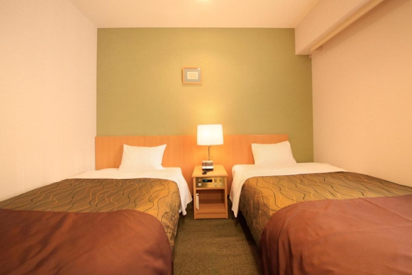 A hotel room with two single beds, a nightstand with a lamp, and a small table.