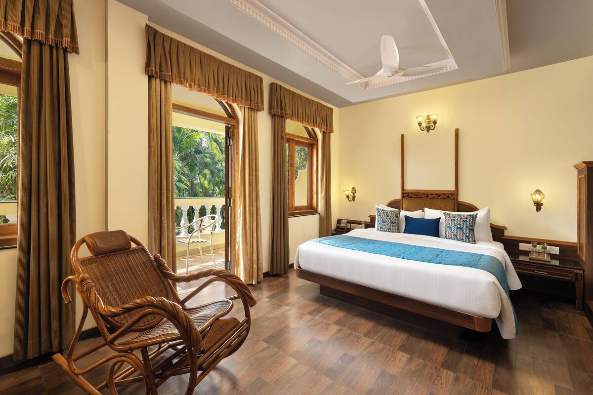 A hotel room with a large bed, a wooden rocking chair, and a balcony with curtains.