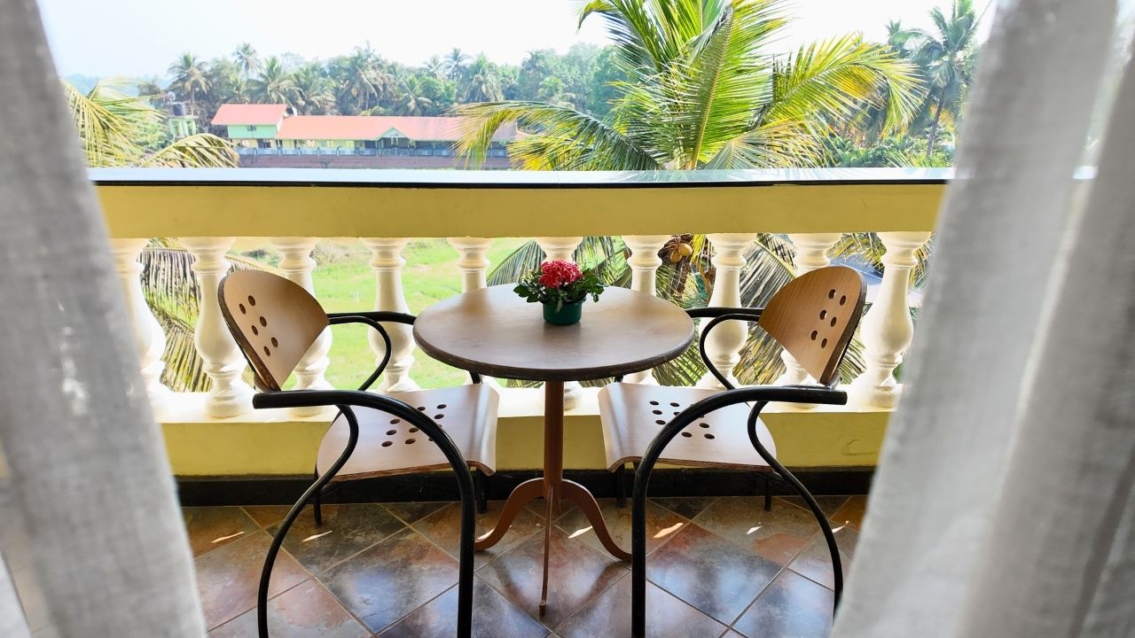 A balcony with two chairs and a small table, a potted plant, and a view of palm trees and buildings.