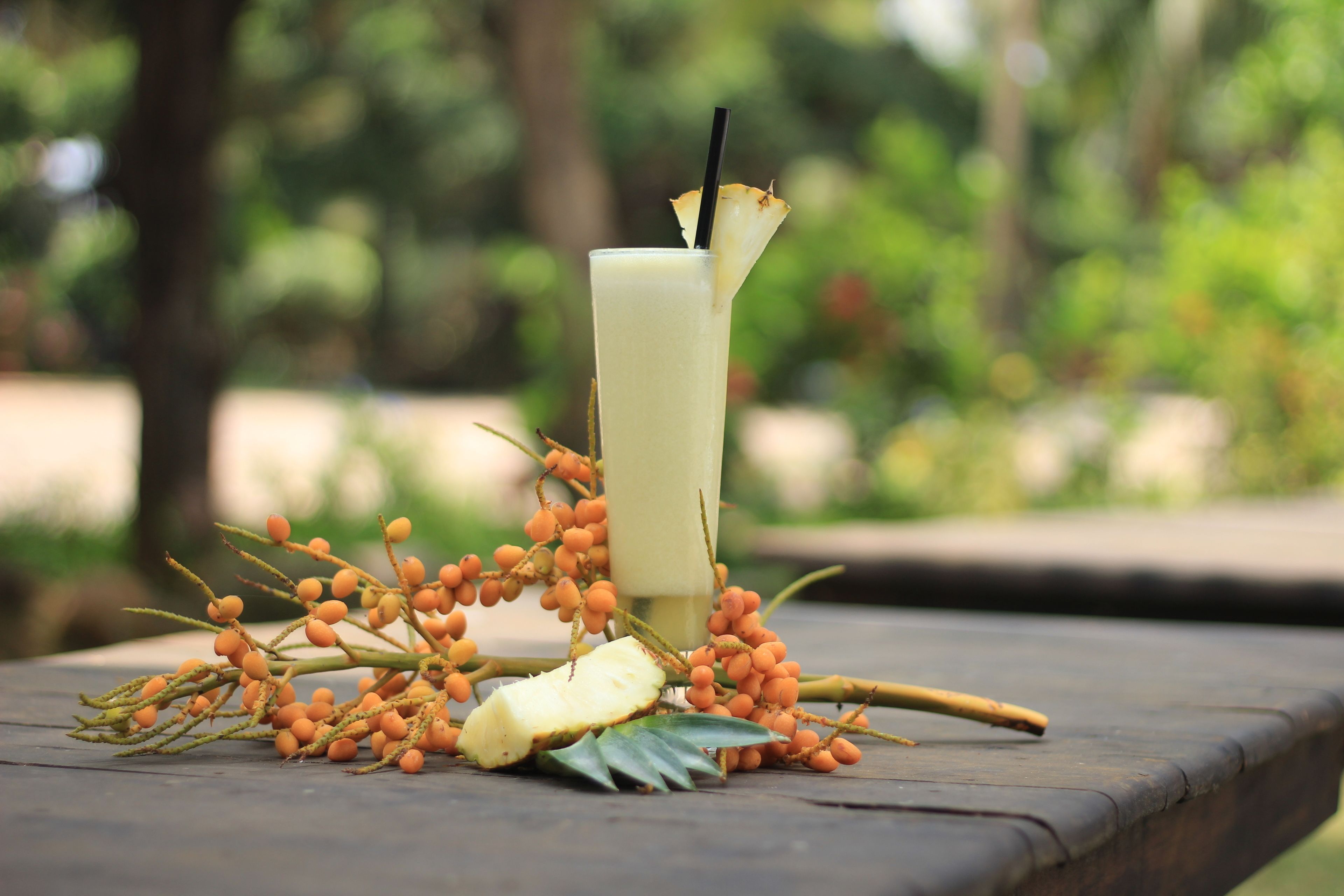 A drink with a straw and a slice of pineapple on a table with a tropical arrangement of fruits and leaves.