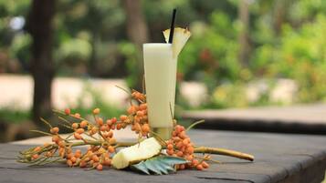 A drink with a straw and a slice of pineapple on a table with a tropical arrangement of fruits and leaves.