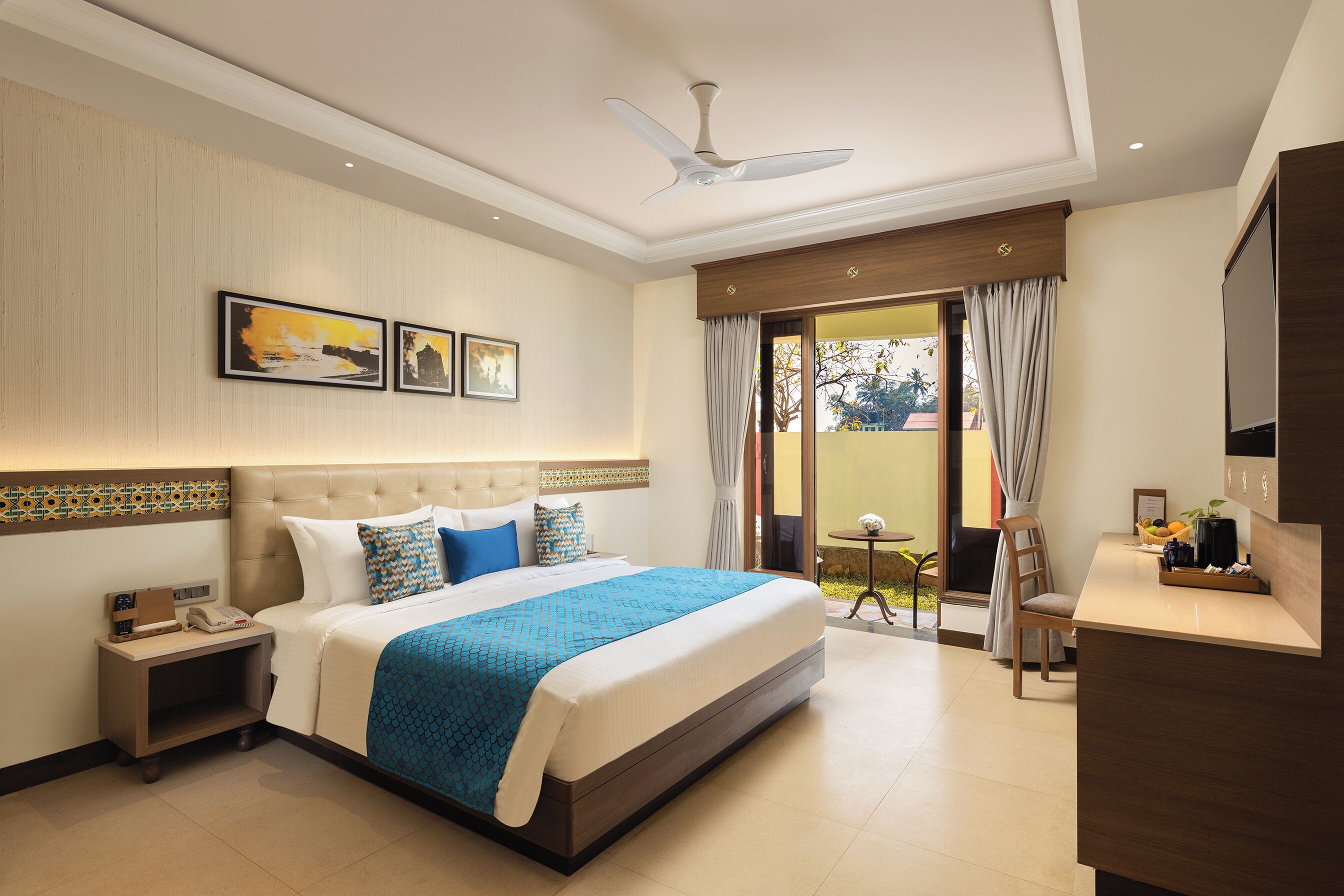 A hotel room with a large bed, a desk, a chair, a ceiling fan, and a view of the outdoors.