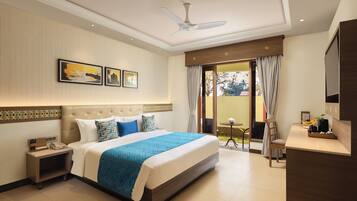 A hotel room with a large bed, a desk, a chair, a ceiling fan, and a view of the outdoors.