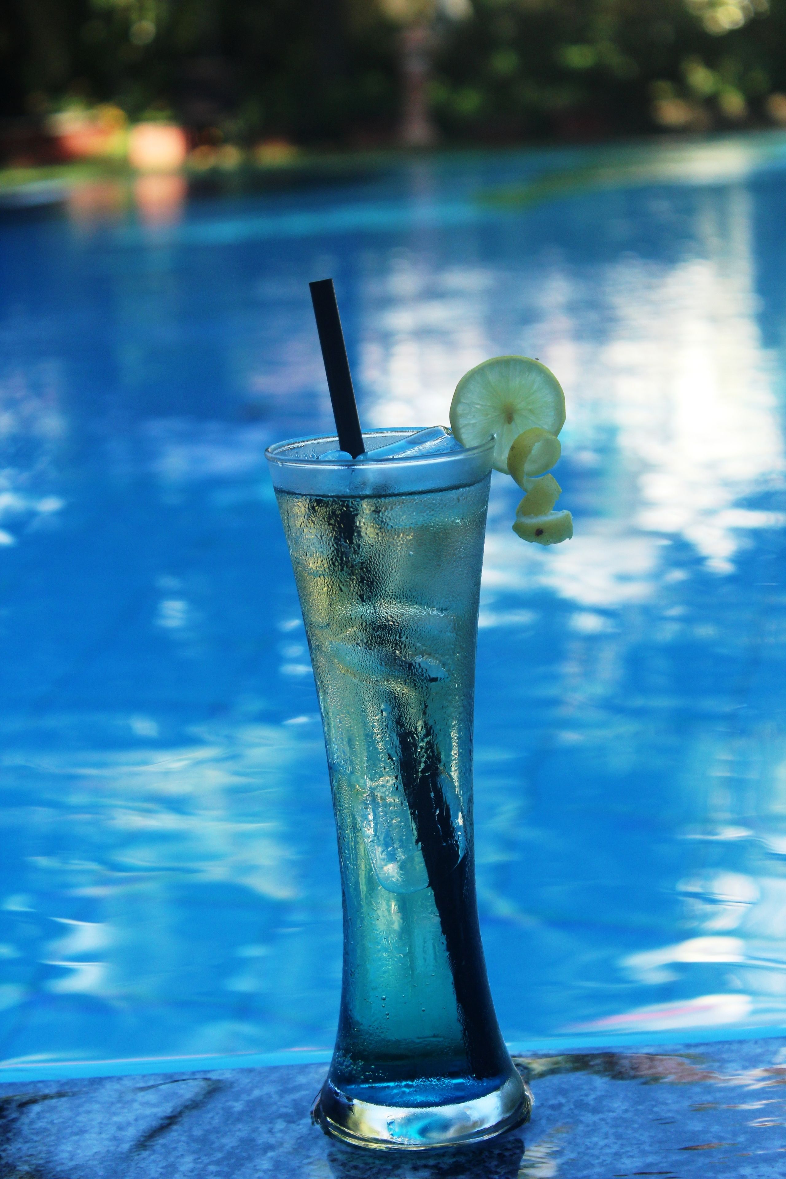 A tall glass with a straw and a slice of lime on a poolside table.