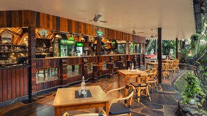 A restaurant with wooden interior and stone flooring, featuring tables and chairs, and a bar area with shelves of bottles. - Fortune Resort Benaulim Goa - Member ITC Hotels' Group (Benaulim)