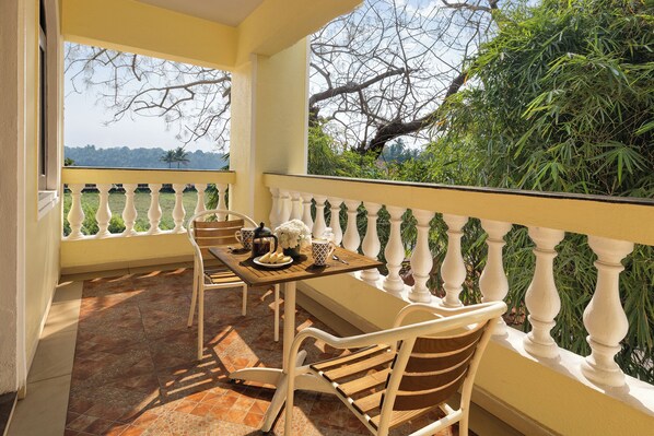 A balcony with a table set for two, white chairs, and a view of greenery and trees.