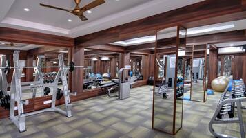 A gym with mirrored walls, ceiling fans, and various exercise equipment.