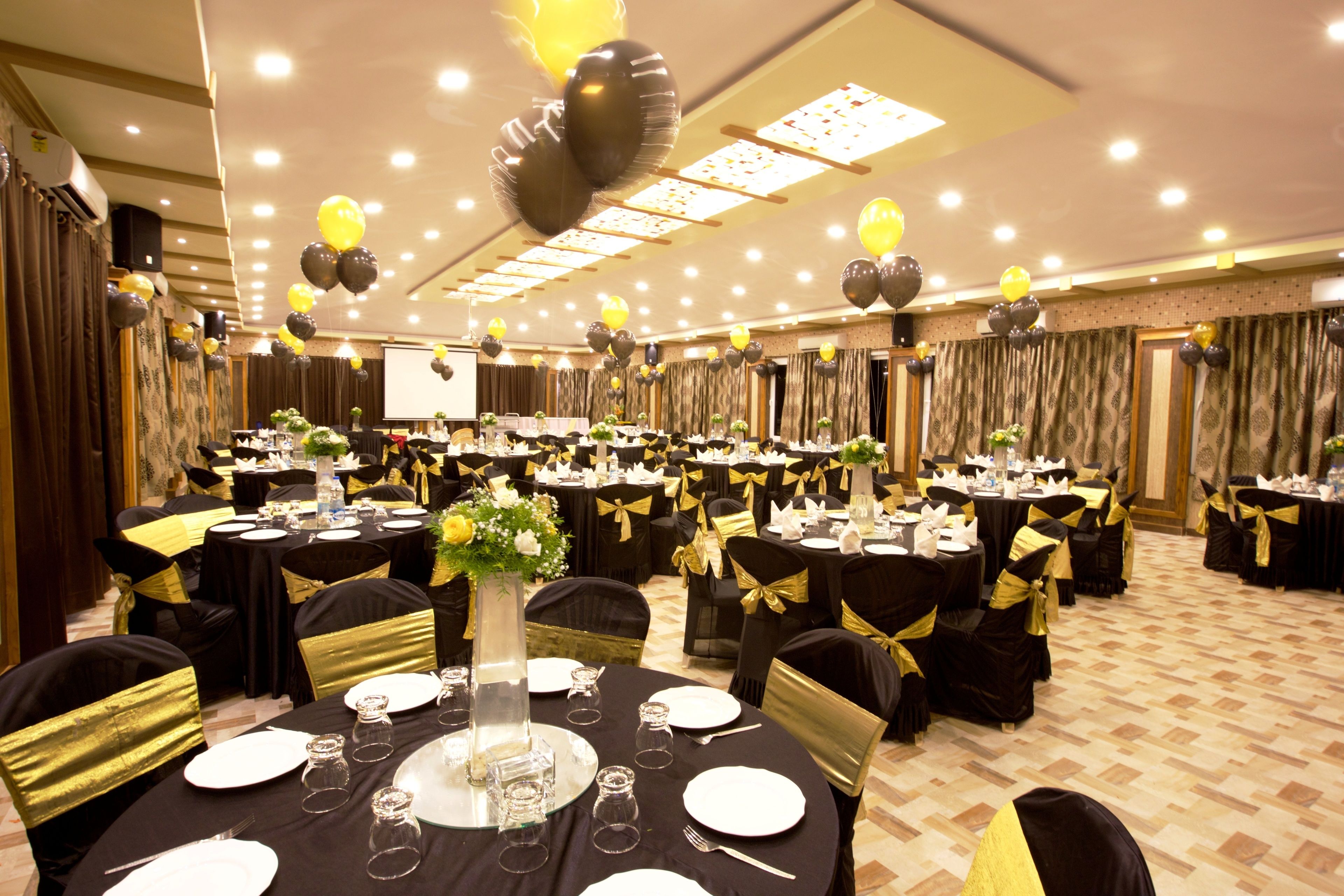Une salle de banquet avec des tables rondes, une décoration aux couleurs noir et or, et un écran de projection.
