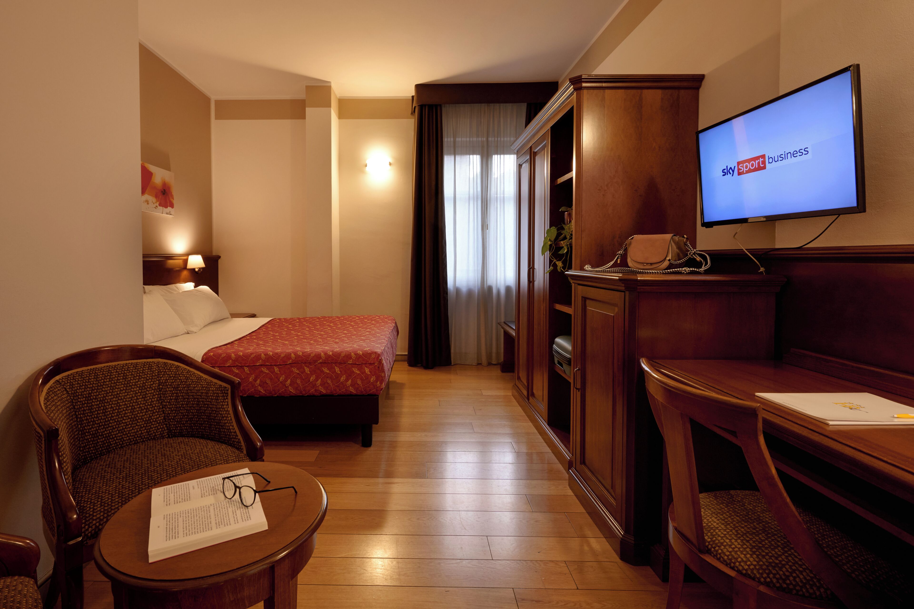 A hotel room with a bed, a desk, a chair, a television, and a wardrobe.