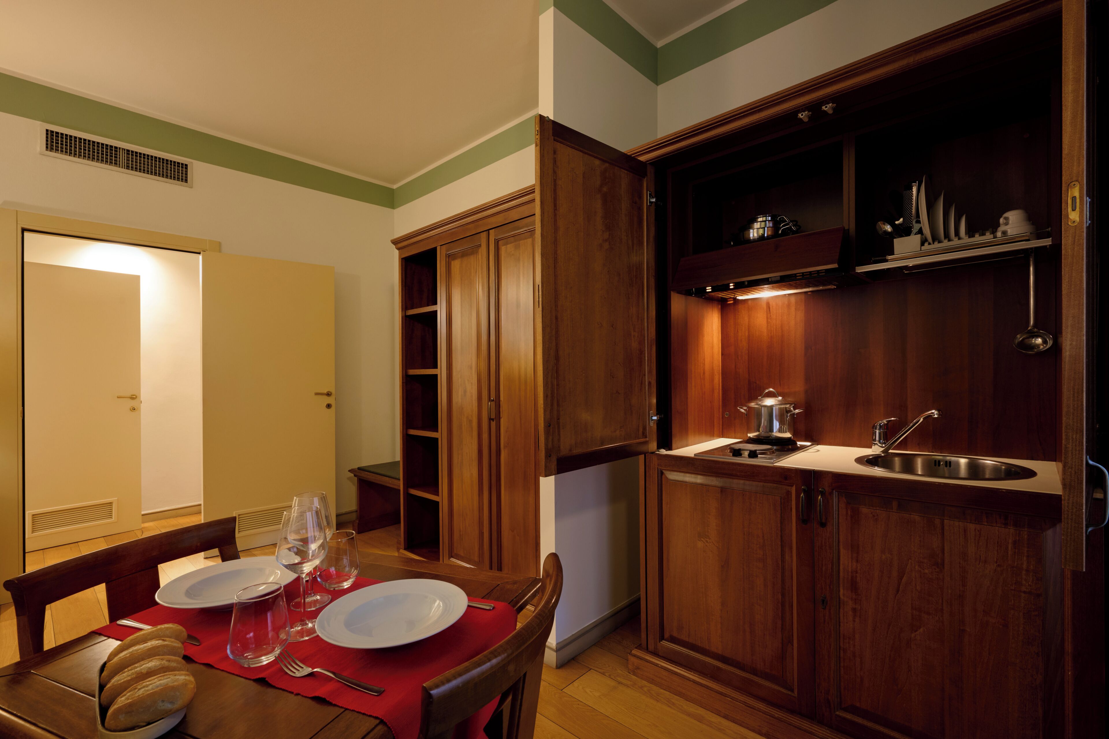A dining area with a table set for two, a wooden cabinet with a sink, and a door leading to another room.
