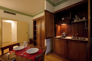 A dining area with a table set for two, a wooden cabinet with a sink, and a door leading to another room.