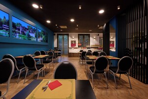 A conference room with tables and chairs, a large window with a view, and a wall-mounted display.