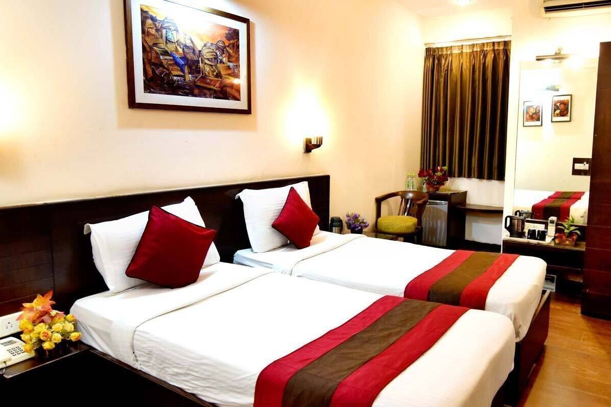 A hotel room with two beds, a desk, a wardrobe, a television, and a painting on the wall.